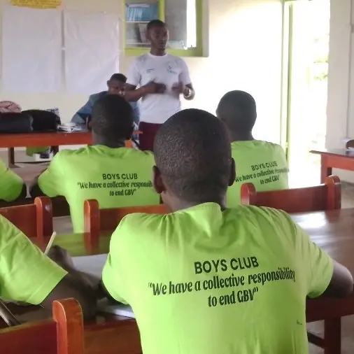 Members of a youth club, in shirts reading “We have a collective responsibility to end GBV”, listening to a facilitator