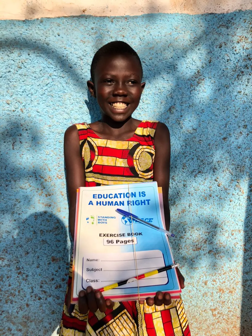 A smiling girl holding up a new exercise book that reads “Education is a human right”