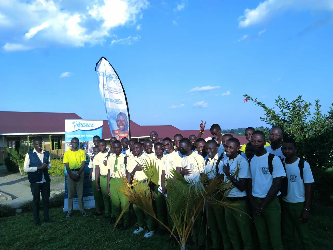 Students in school uniform gathered outdoors with VPEACE volunteers beside a VPEACE banner